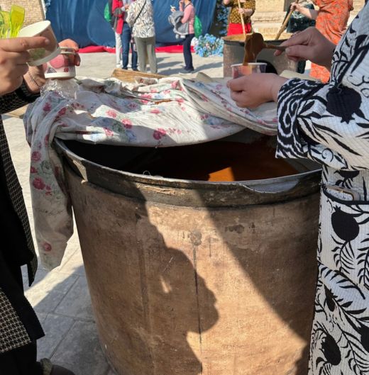 Serving up a cup of sumulak while women stir another cauldron.
